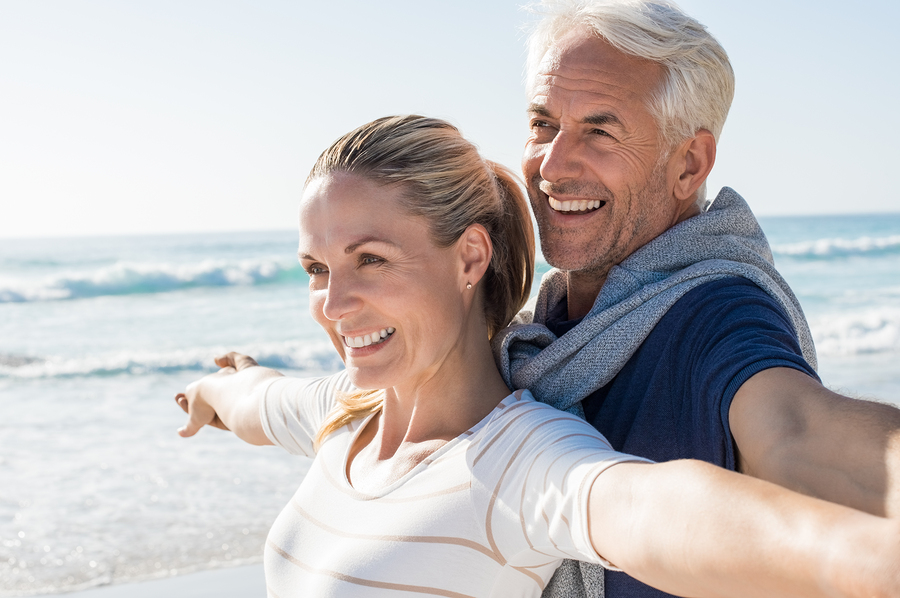Happy senior couple standing on beach with arms outstretched and